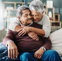 Older woman hugging an older man in their living room.