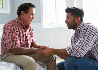 Younger and older man talking while holding hands.